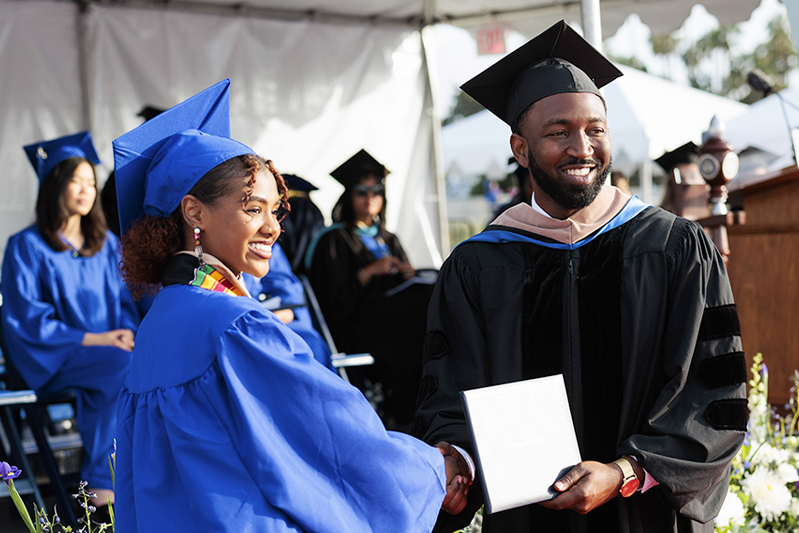 Graduate smiling with board of trustee member.