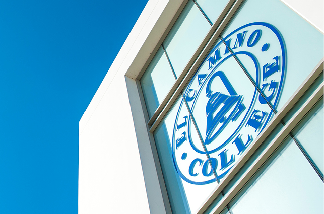 El Camino College logo displayed on the window of a white building with a blue sky background.
