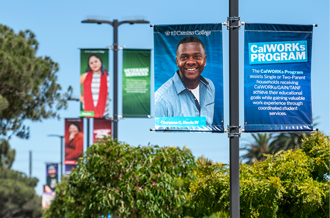 A row of vertical campus banners displayed on outdoor light poles at El Camino College. The banners feature various promotional designs, including one highlighting the CalWORKs Program with text describing support for students in single‑ or two‑parent households. Additional colorful banners appear in the background, surrounded by trees and a clear sky.