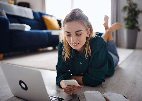 Woman looking on phone while laying on the floor in front of her laptop